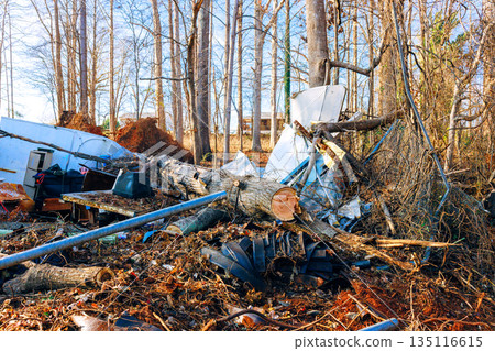 Vacant lot shows scattered debris, fallen trees, equipment among dry leaves branches in winter. 135116615
