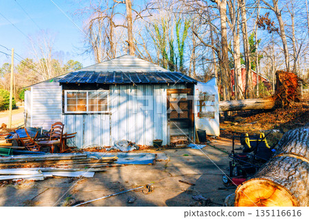 Small, worn building stands amidst trees with scattered items around it during winter. 135116616