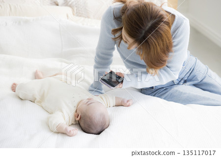 A young mother taking a photo of her baby with a smartphone 135117017