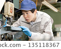 Young man working on a drill press in a factory 135118367
