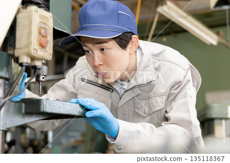 Young man working on a drill press in a factory Young man working on a drill press in a factory 135118367