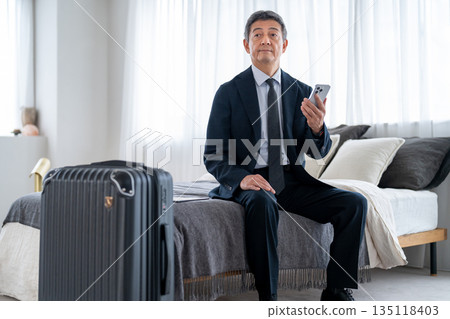 A senior man who arrives at a hotel on a business trip and checks his smartphone 135118403