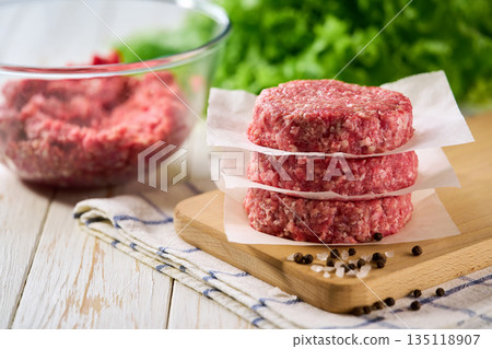 Raw beef burger patties one above other on a white table. Raw beef burger patties one above other on a white table. 135118907