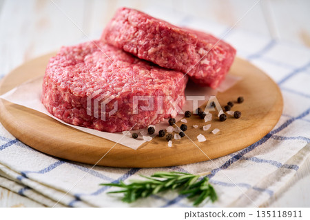 Two raw beef burger patties with peppers and salt on a white table. Ideal ingredient for grill, BBQ . Two raw beef burger patties with peppers and salt on a white table. Ideal ingredient for grill, BBQ . 135118911