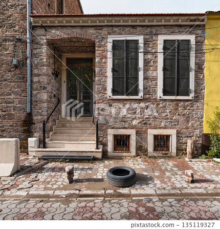 Traditional stone house facade with ornate door and closed windows on a cobblestone street in Izmir, Turkey. Traditional stone house facade with ornate door and closed windows on a cobblestone street in Izmir, Turkey. 135119327