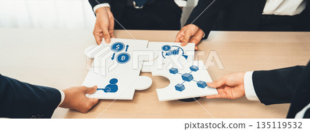 Business team assembling puzzle pieces with icons representing finance, strategy, and growth concepts in a collaborative workplace environment. Amity 135119532