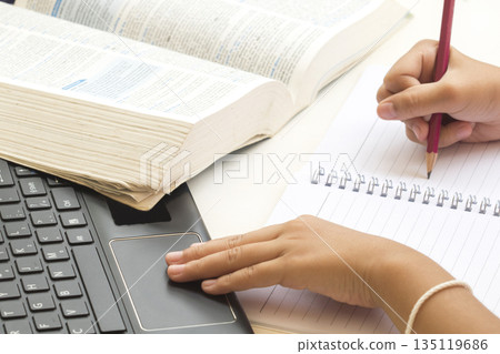 student girl writing notebook with dictionary book and computer for study  135119686