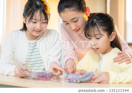 Elementary school girls enjoying exchanging stickers using a sticker book after school 135121544