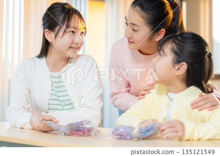 Elementary school girls enjoying exchanging stickers using a sticker book after school Elementary school girls enjoying exchanging stickers using a sticker book after school 135121549