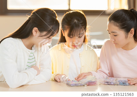 Elementary school girls enjoying exchanging stickers using a sticker book after school Elementary school girls enjoying exchanging stickers using a sticker book after school 135121563