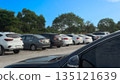Outdoor parking lot filled with various cars under a bright blue sky and green trees background. Transportation and travel concept. 135121639