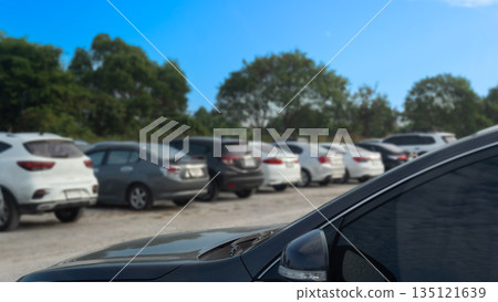 Outdoor parking lot filled with various cars under a bright blue sky and green trees background. Transportation and travel concept. Outdoor parking lot filled with various cars under a bright blue sky and green trees background. Transportation and travel concept. 135121639
