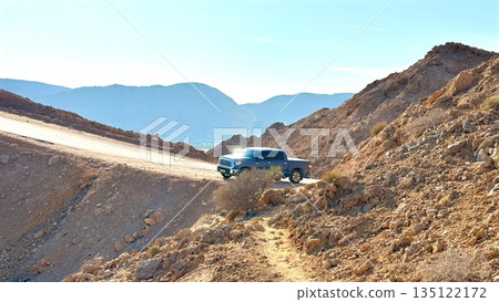 Blue Suv Perched On Rocky Slope, Overlooking Desert Canyon At Golden Hour, Rugged Vehicle With Open Trunk, Spare Tire Visible, Dust Trail, Solitary Outdoor Scene Evoking Freedom And Exploration Blue Suv Perched On Rocky Slope, Overlooking Desert Canyon At Golden Hour, Rugged Vehicle With Open Trunk, Spare Tire Visible, Dust Trail, Solitary Outdoor Scene Evoking Freedom And Exploration 135122172