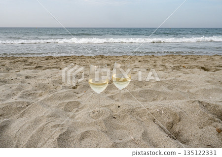 Two Glasses of Wine at the Beach in romantic setting in Corsica, France looking on the Ocean waves front blue cloudy sky Two Glasses of Wine at the Beach in romantic setting in Corsica, France looking on the Ocean waves front blue cloudy sky 135122331