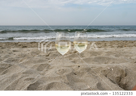Two Glasses of Wine at the Beach in romantic setting in Corsica, France looking on the Ocean waves front blue cloudy sky Two Glasses of Wine at the Beach in romantic setting in Corsica, France looking on the Ocean waves front blue cloudy sky 135122333