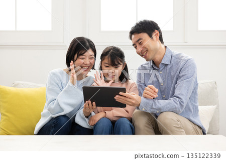 一家三口面帶笑容,正在用平板電腦進行視訊通話。 一家三口面帶笑容,正在用平板電腦進行視訊通話。 135122339