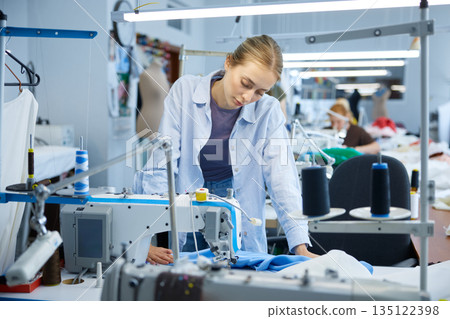 Young seamstress inspecting and ensuring quality of industrial sewing work 135122398
