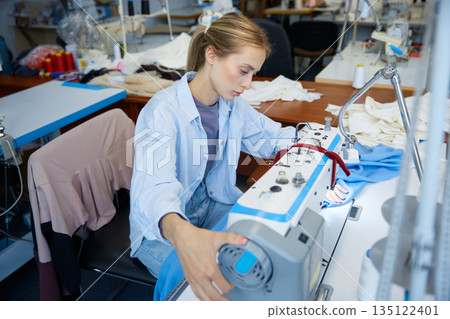 Seamstress expertly managing fabric through industrial sewing process 135122401