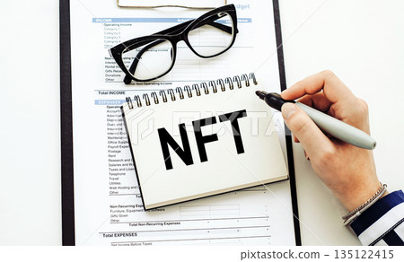 NFT text, written on a note book with eyeglasses 135122415