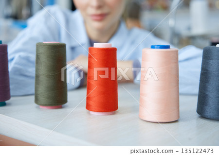 Craftswoman surrounded by colorful threads and machines. 135122473