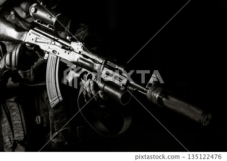 Man in black uniform aiming with silenced Kalashnikov assault rifle on black background Man in black uniform aiming with silenced Kalashnikov assault rifle on black background 135122476