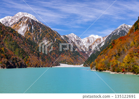 長野縣大町市平良－高瀨水壩調節湖的秋葉呈現出鮮豔的乳藍色，遠處是白雪皚皚的山峰，映襯著蔚藍的天空。 135122691