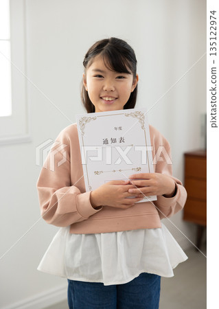 An elementary school girl holding a report card and looking anxious 135122974