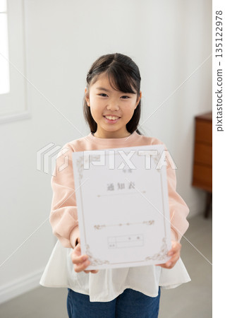 An elementary school girl holding a report card and looking anxious An elementary school girl holding a report card and looking anxious 135122978
