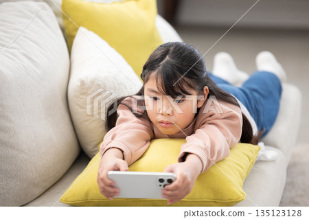 An elementary school girl lying on the sofa and operating a smartphone An elementary school girl lying on the sofa and operating a smartphone 135123128