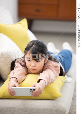 An elementary school girl lying on the sofa and operating a smartphone An elementary school girl lying on the sofa and operating a smartphone 135123129
