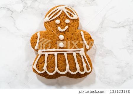A single decorated gingerbread girl cookie on a marble countertop, showcasing its intricate royal icing dress and smiling face. 135123188