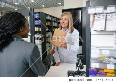 Female customer talking to a pharmacist at the cashier desk 135123203