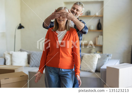 Senior man covering woman eyes in cozy living room with cardboard boxes 135123213