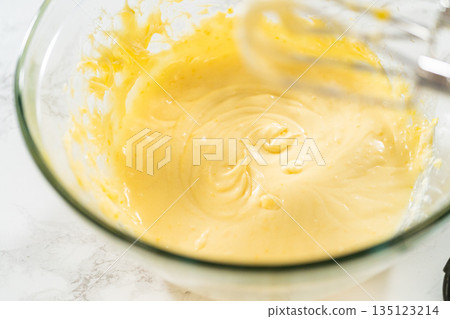 A close-up of whipped butter and sugar in a glass mixing bowl, forming a light and fluffy base for lemon spritz cookies. The smooth, creamy texture ensures the perfect consistency for piping delicate 135123214