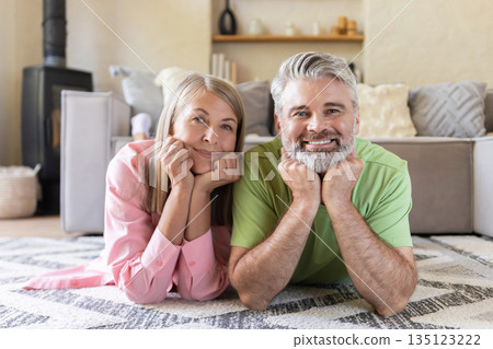 Elderly husband and wife lying on patterned rug 135123222