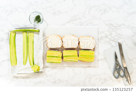 Cucumber slices added to cream cheese covered bread in the Mini Cucumber Sandwiches recipe. Ideal for sandwich tutorials, recipe blogs, or step-by-step visuals. Cucumber slices added to cream cheese covered bread in the Mini Cucumber Sandwiches recipe. Ideal for sandwich tutorials, recipe blogs, or step-by-step visuals. 135123257