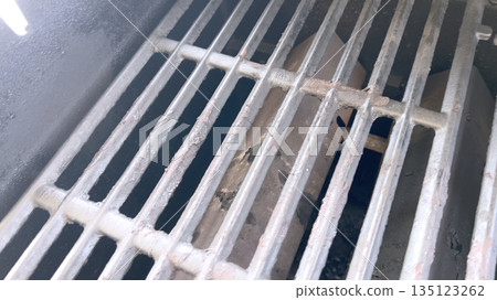 Top-down image of grill grates stained with dark grease and burned food particles. The metal bars show signs of heavy use and discoloration. Top-down image of grill grates stained with dark grease and burned food particles. The metal bars show signs of heavy use and discoloration. 135123262