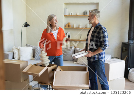 Husband and wife unpacking together cardboard boxes in living room Husband and wife unpacking together cardboard boxes in living room 135123266