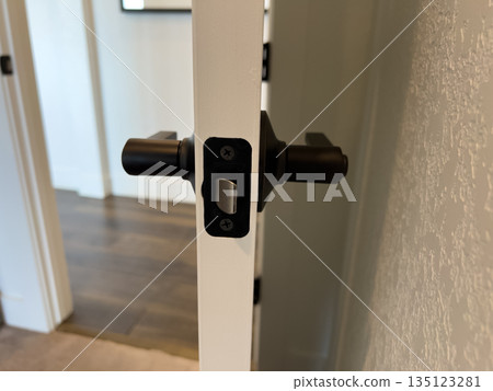 A close-up view of a black matte interior latch on a white residential door. The clean and modern hardware is shown in sharp detail against a neutral backdrop. 135123281