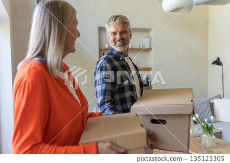 Couple enjoying moving into new home holding boxes Couple enjoying moving into new home holding boxes 135123305