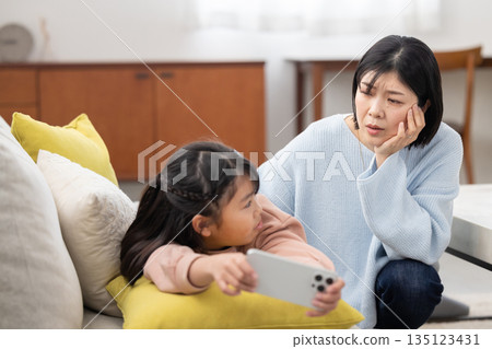 一位母親焦急地看著正全神貫注於智慧型手機的女兒。 一位母親焦急地看著正全神貫注於智慧型手機的女兒。 135123431