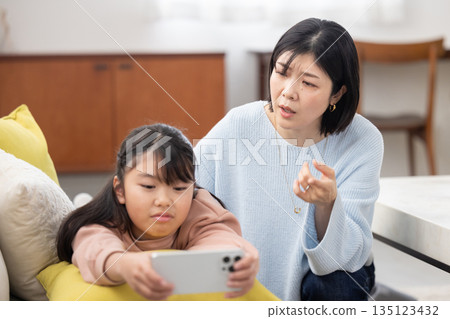 一位母親焦急地看著正全神貫注於智慧型手機的女兒。 135123432