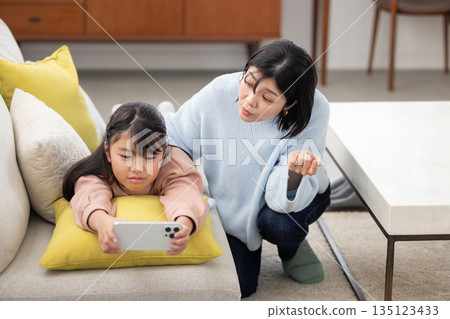 A mother looks anxiously at her daughter who is engrossed in her smartphone 135123433