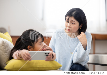 A mother looks anxiously at her daughter who is engrossed in her smartphone 135123434