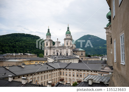 Panoramic view of Salzburg old town rooftops with cathedral towers and green alpine hills in background 135123683