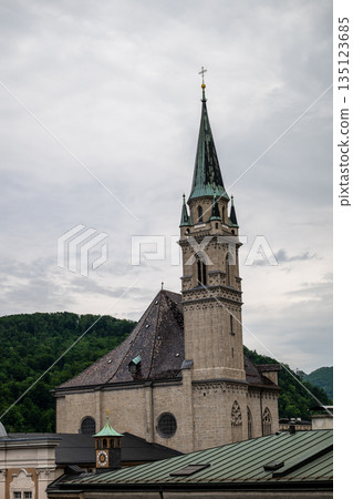 Historic church tower rising above Salzburg old town rooftops with green alpine hills in background 135123685