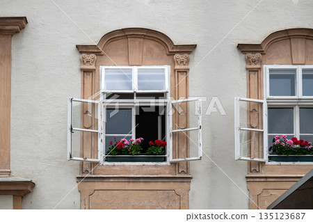 Open historic window with colorful flower boxes on classic European building facade in old town setting 135123687