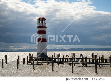 Red and white striped Podersdorf Lighthouse Austria standing on wooden pier under dramatic cloudy sky Red and white striped Podersdorf Lighthouse Austria standing on wooden pier under dramatic cloudy sky 135123692