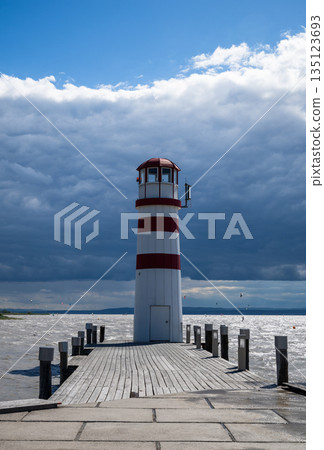 Red and white striped Podersdorf Lighthouse Austria standing on wooden pier under dramatic cloudy sky 135123693