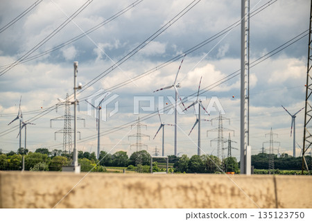 Wind turbines and power lines across rural landscape under blue sky for renewable energy generation Wind turbines and power lines across rural landscape under blue sky for renewable energy generation 135123750